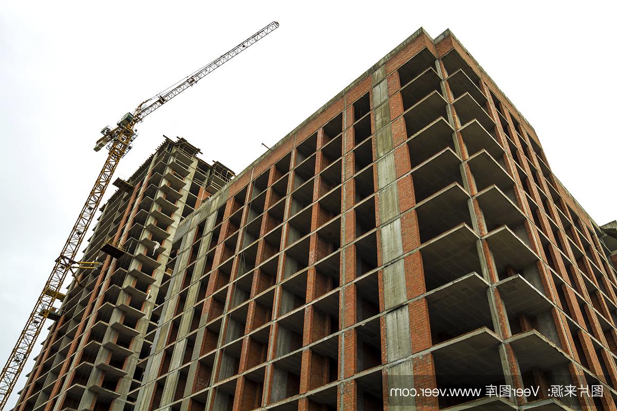 A ground view of a modern residential building under construction。Real estate development concept。A multi-storey house made of brick and concrete。A tower crane is working at the construction site。